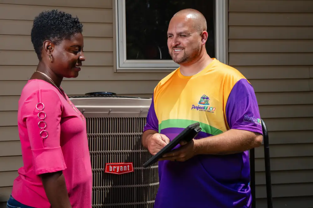 Heat pump installation costs explained - Perfect Temp technician holding a clipboard while standing next to a woman & a newly installed heat pump.